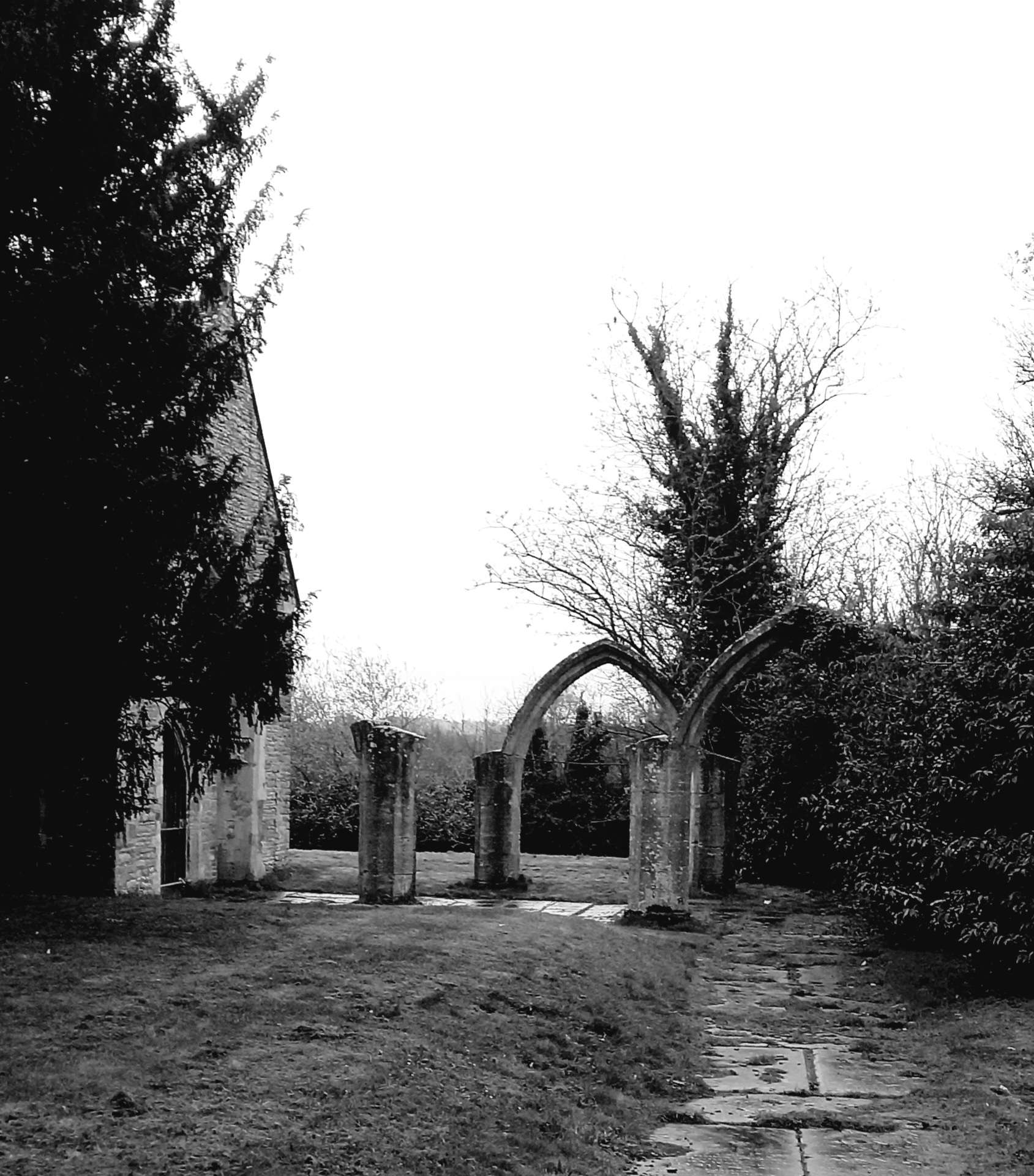 The wreck of two bowtopped doorways next to an old church mostly hidden by trees.