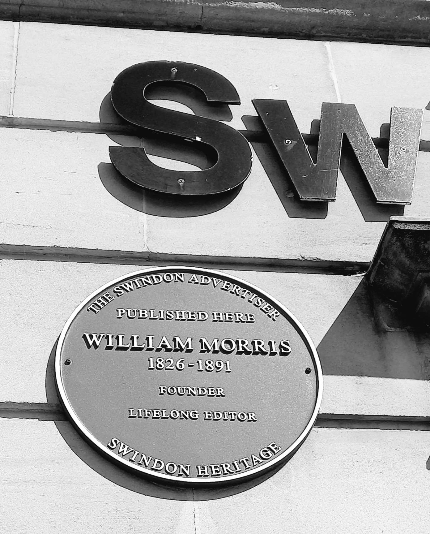 A marker saying 'William Morris 1826-1891 Founder', on the side of the old Swindon Adver building.